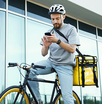 Express delivery courier with insulated bag looking at phone on bicycle.