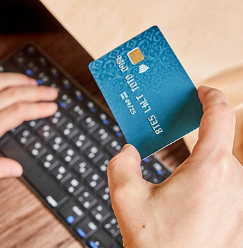 Image of hand holding credit card in front of keyboard.
