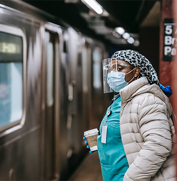 Image of nurse in protective mask and coat waiting for train on subway station.