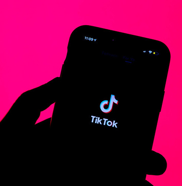 Silhouette image of hand holding smartphone with TikTok logo.