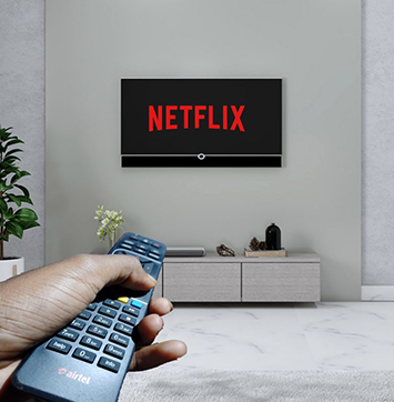 Image of Netflix logo on TV screen with hand holding remote in foreground.