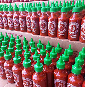 Image of rows of sriracha hot sauce bottles.