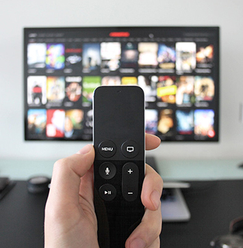 Image of hand holding Apple TV remote with tv in background.